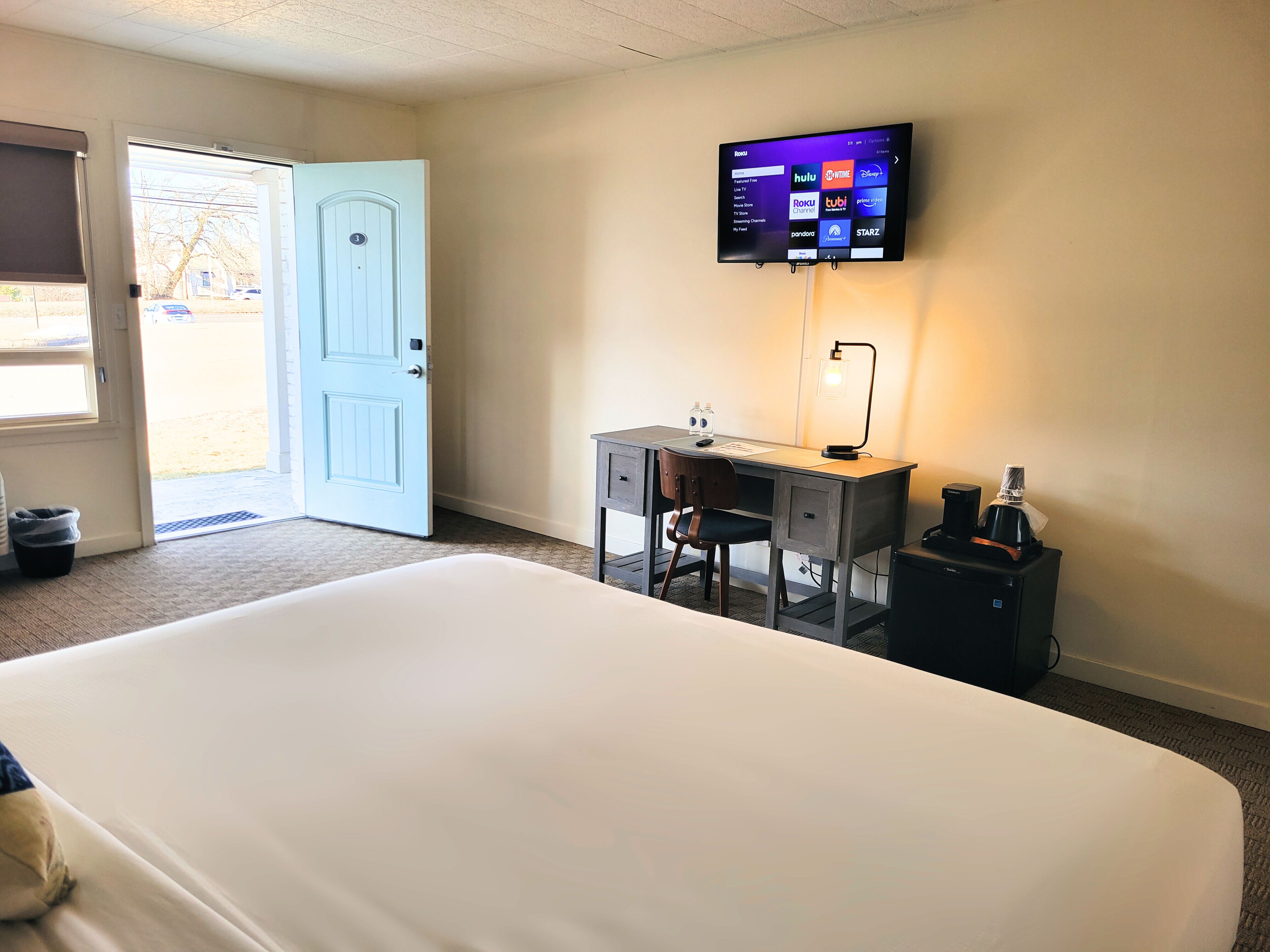 A hotel room with a bed, desk, chair, television, and a coffee maker.