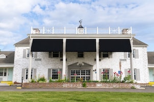 A white building with a balcony, a weather vane, and a brick facade.