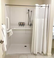 A shower area with a white curtain, a handheld showerhead, and a wall-mounted faucet.
