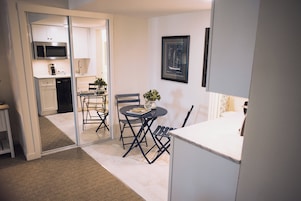 Una cocina compacta con microondas, un pequeño comedor con mesa y sillas, y una puerta corredera que da a un baño.