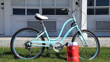 A turquoise bicycle with a white seat and 'COWNIE' branding, parked on grass in front of a white building with large windows and vents.