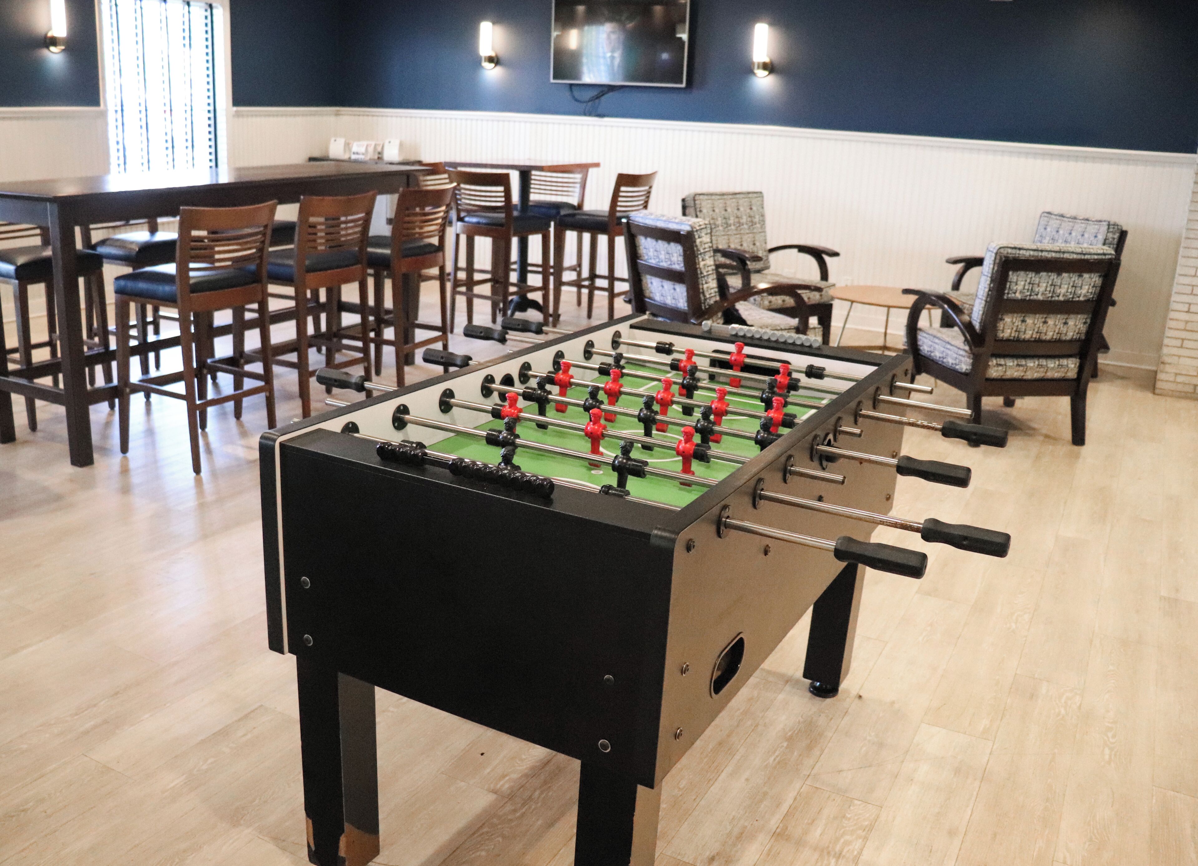 A foosball table in a room with wooden chairs and a television mounted on the wall.