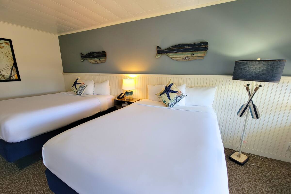 Habitación de hotel con dos camas, una mesita de noche con lámpara, decoración de peces en la pared y una almohada con forma de estrella de mar.