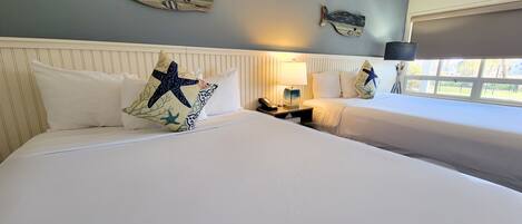 A hotel room with two beds, a nightstand with a lamp, and decorative fish wall art.