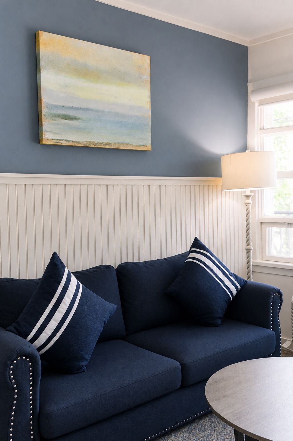 A room with a navy blue sofa, a white paneled wall, and a painting above the sofa.