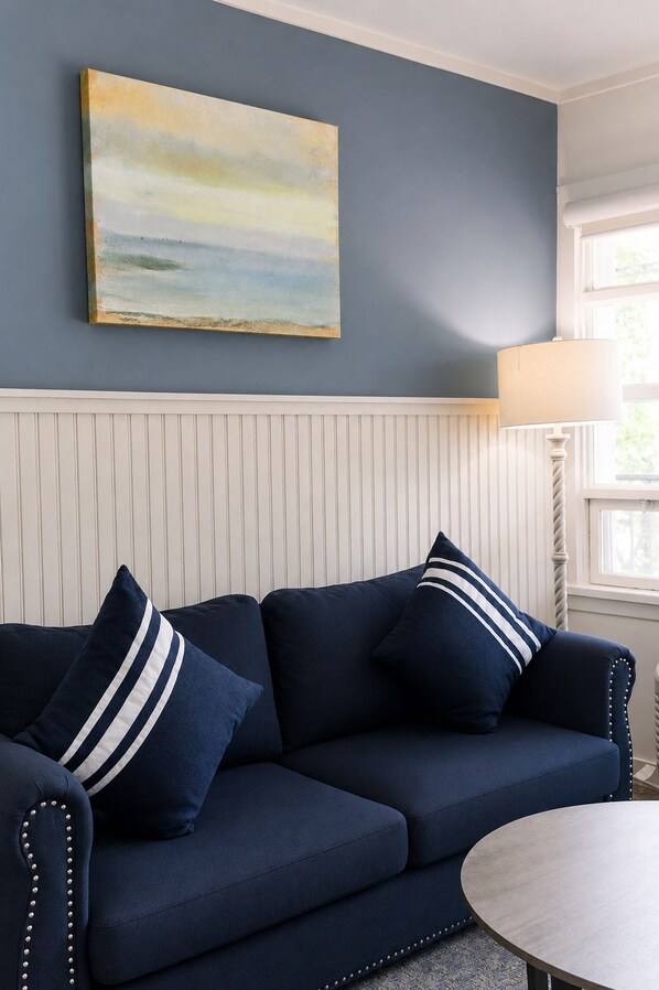 A room with a navy blue sofa, a white paneled wall, and a painting above the sofa. - The Circle Hotel Fairfield (Fairfield)