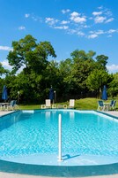 A clear blue swimming pool with lounge chairs and umbrellas, surrounded by trees.
