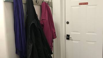 A hallway with a white door marked "Emergency Exit" and a coat rack with several coats.