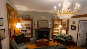 A living room with a fireplace, bookshelves, a chandelier, and leather furniture. - Pring Guesthouse - Hostel (Hamilton)