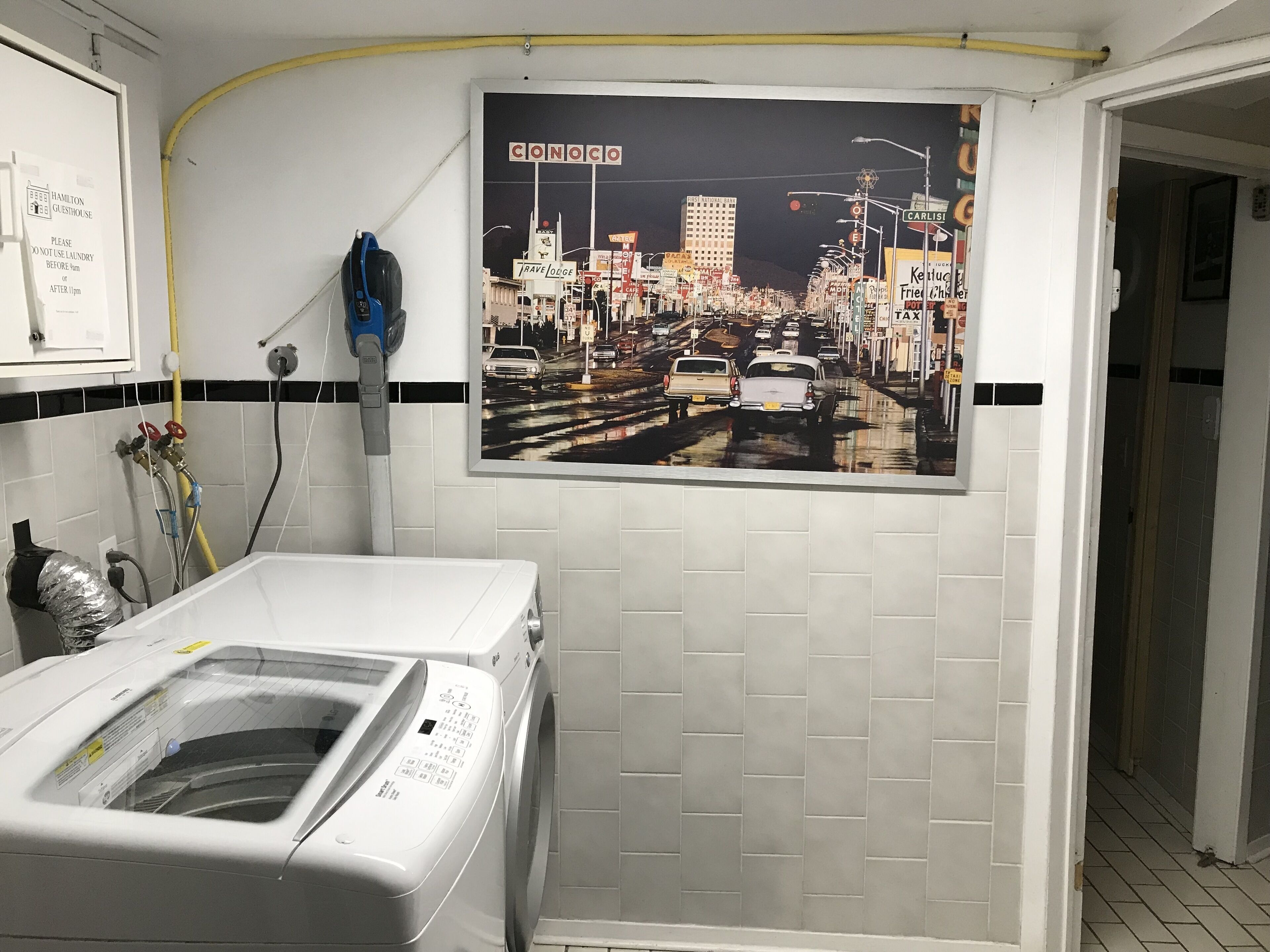 A hotel room with a large poster of a cityscape, a washing machine, and a sign indicating no laundry use before 11pm.