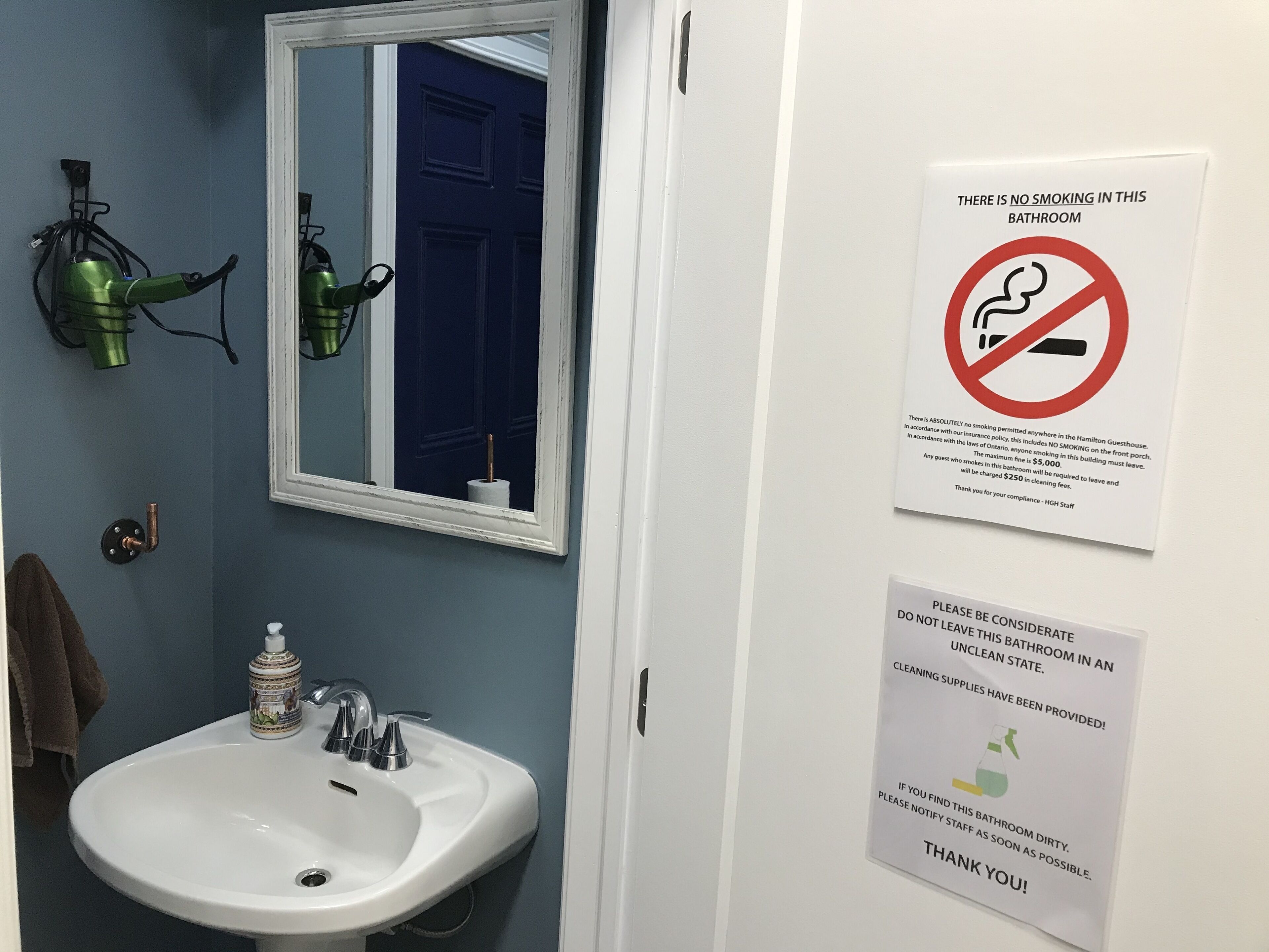 Un baño con lavamanos, espejo y letrero de prohibido fumar.