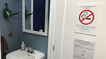 Un baño con lavamanos, espejo y letrero de prohibido fumar.
