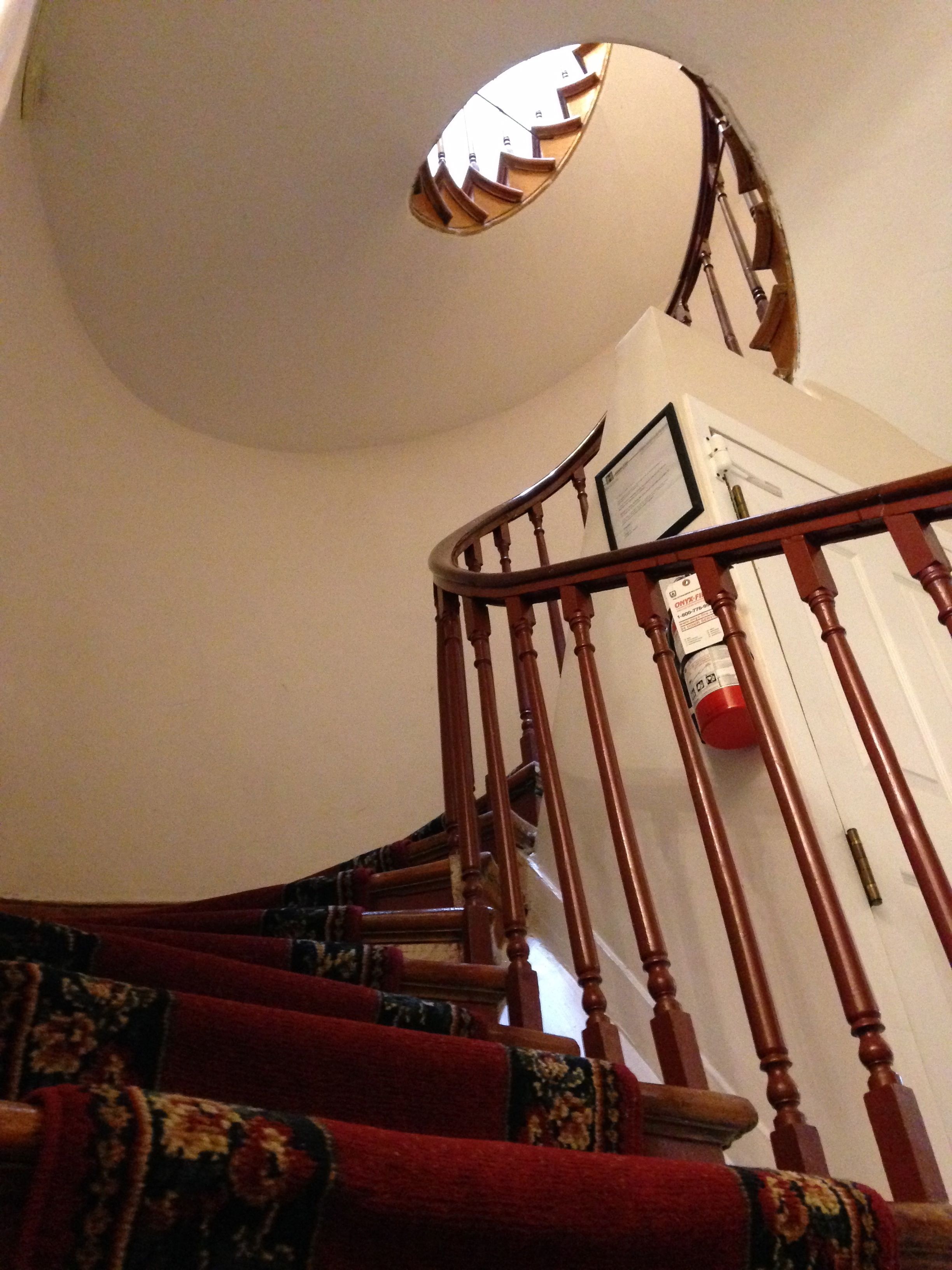A wooden staircase with red carpeted steps and a white wall.