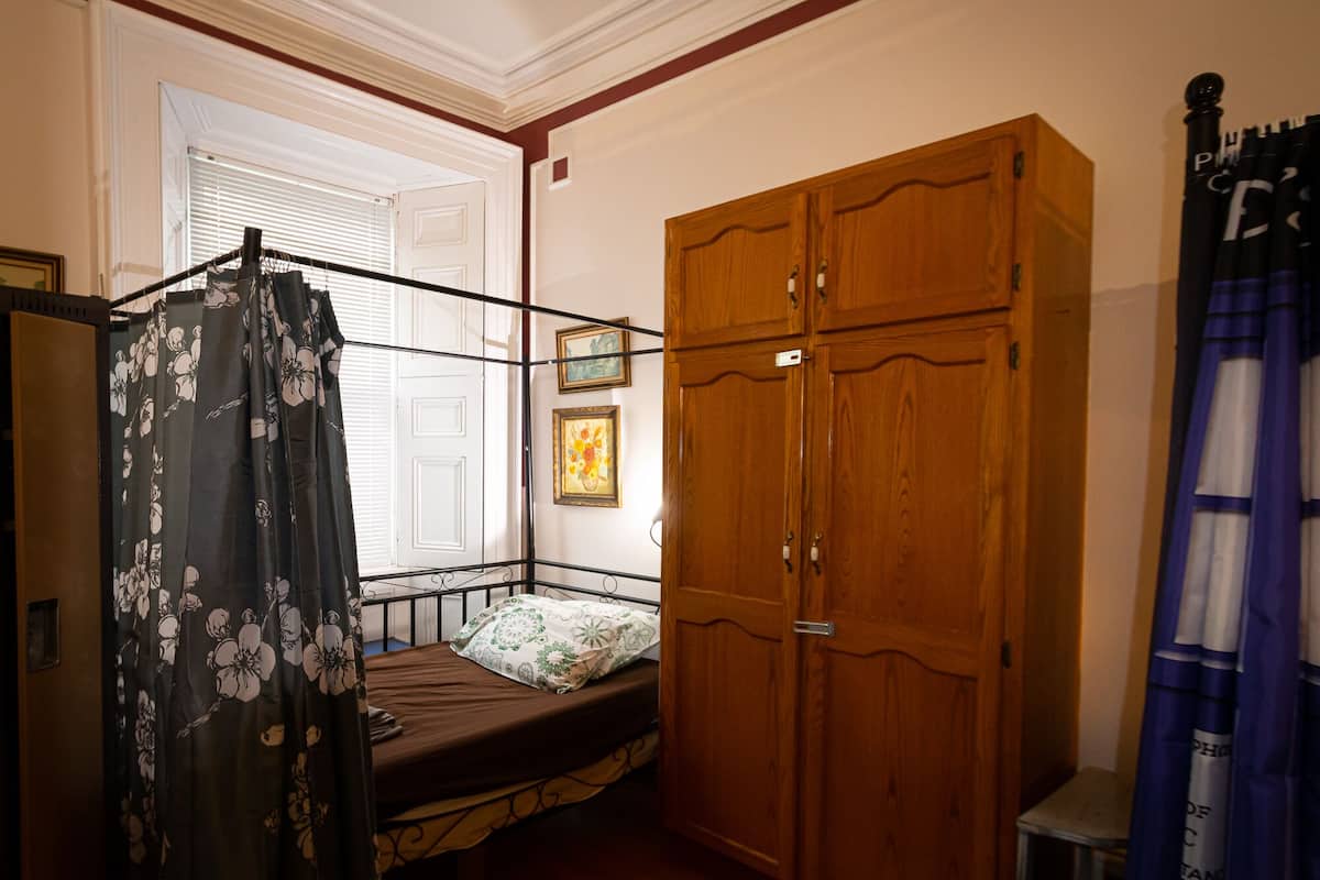 A bedroom with a bed, wooden wardrobe, and a window with curtains.