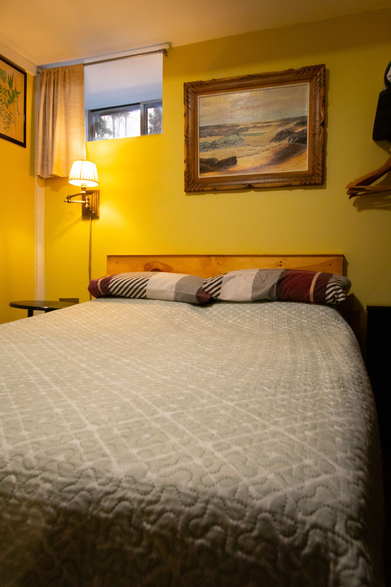 Quarto de hotel com cama, mesa de cabeceira, luminária, quadro na parede e janela com cortinas.