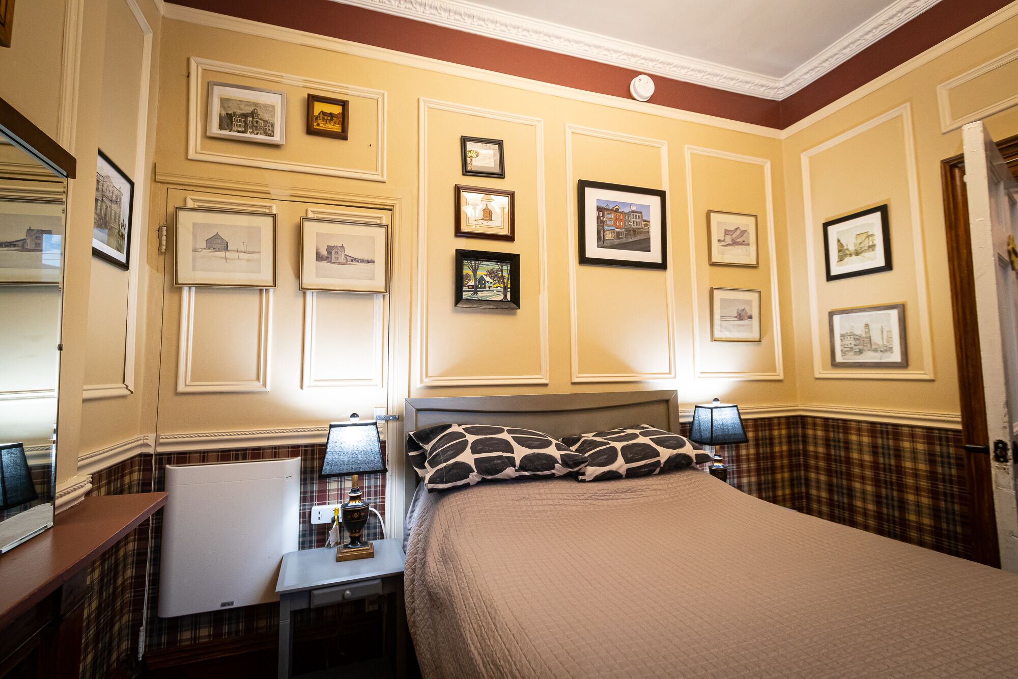 Une chambre d’hôtel avec un lit, des tables de chevet, une lampe et des tableaux encadrés au mur.
