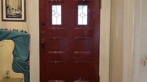 A red door with a glass window, a small framed picture on the wall, and a blue chair in the foreground. - Pring Guesthouse - Hostel (Hamilton)