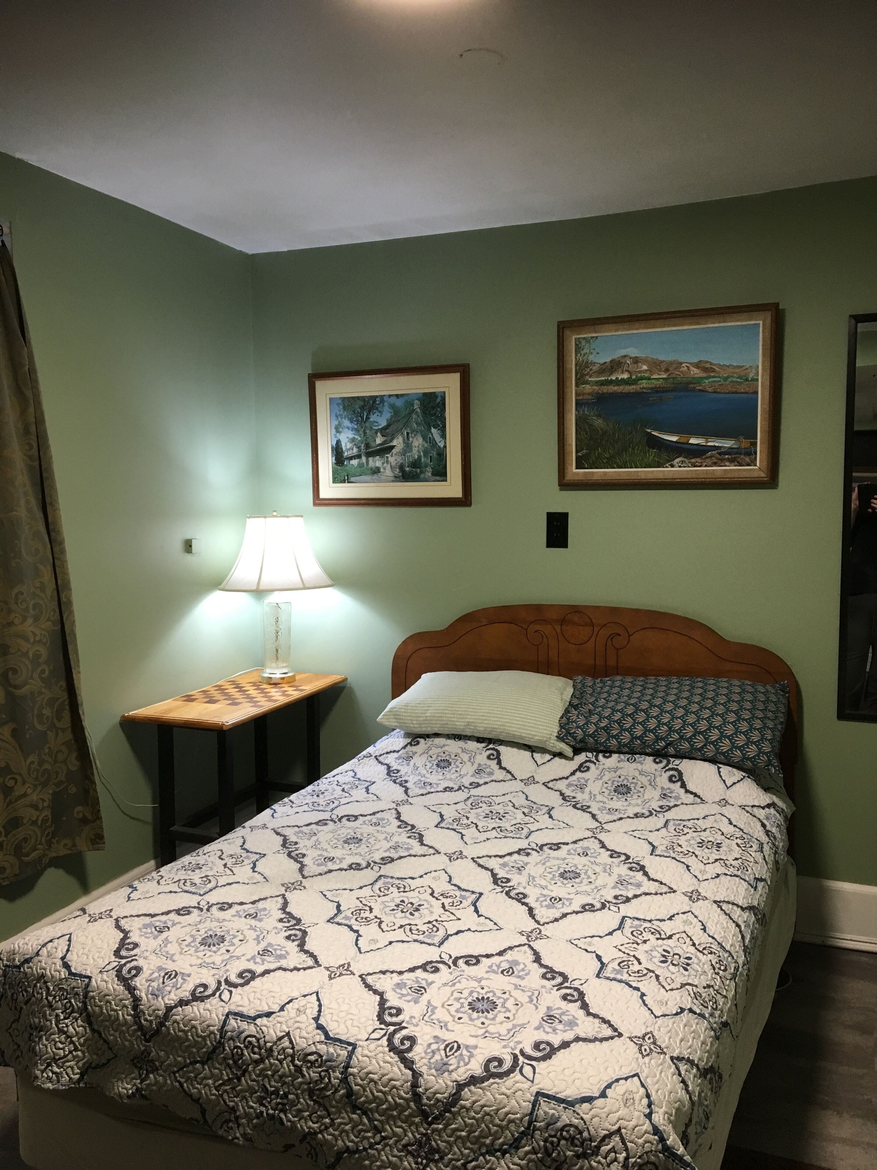 A bedroom with a bed, a nightstand, a lamp, and two framed pictures on the wall.