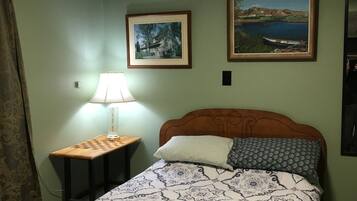 A bedroom with a bed, a nightstand, a lamp, and two framed pictures on the wall.