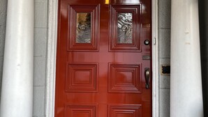 A red door with a glass panel, flanked by white columns, and a security camera above. - Pring Guesthouse - Hostel (Hamilton)
