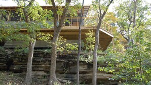 A wooden cabin with a balcony, surrounded by trees and a rocky cliff. - Beaver Lakefront Cabins - Couples Only Getaways (Eureka Springs)