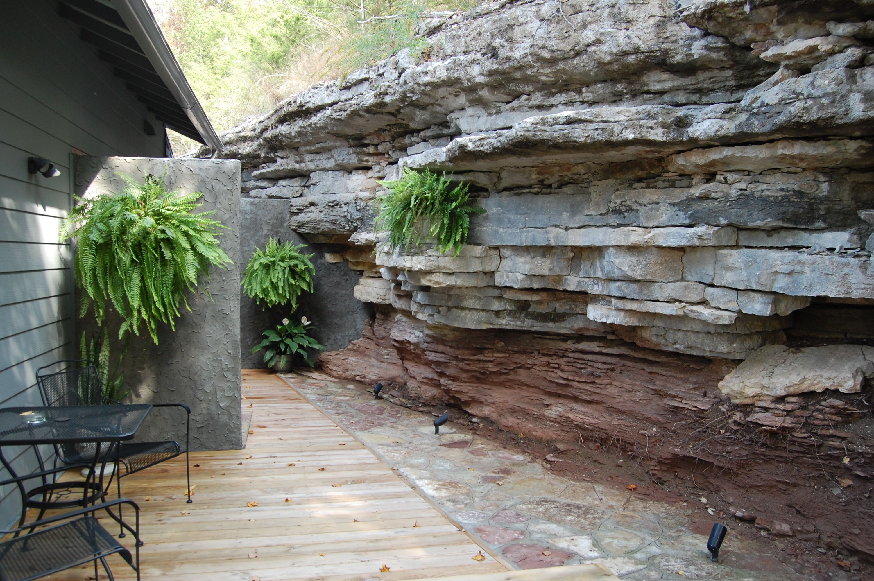 Un patio con muro de piedra, cubierta de madera y dos plantas en macetas.