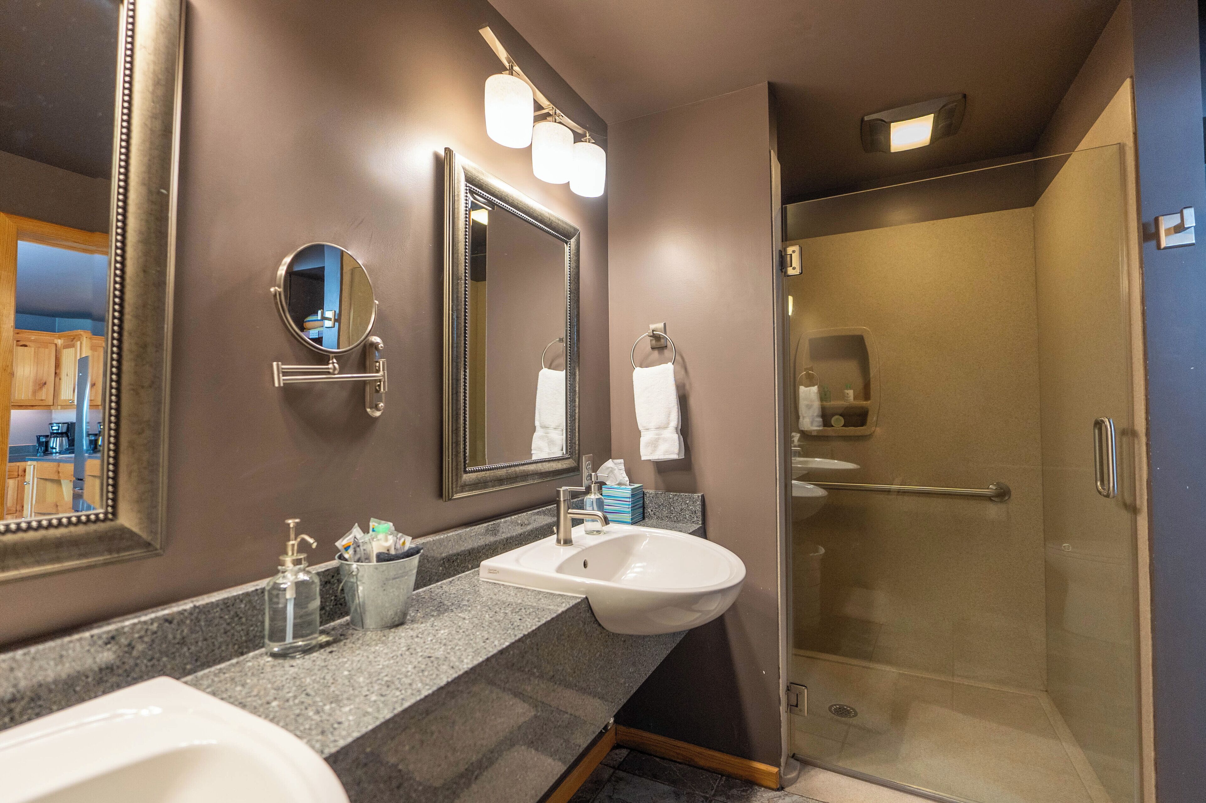 A modern bathroom with a large mirror, a sink, and a glass-enclosed shower.
