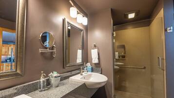 A modern bathroom with a large mirror, a sink, and a glass-enclosed shower.