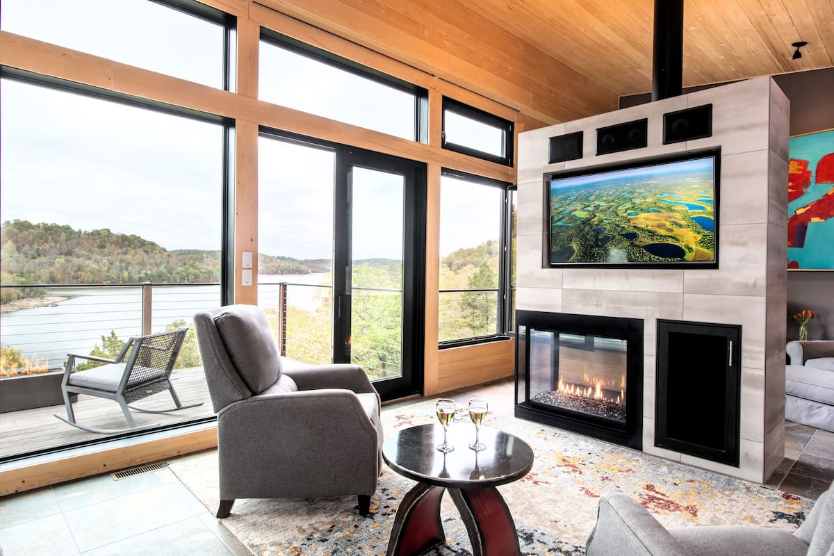 Un salon moderne doté d’un grand téléviseur, d’une cheminée et offrant une vue sur un lac.