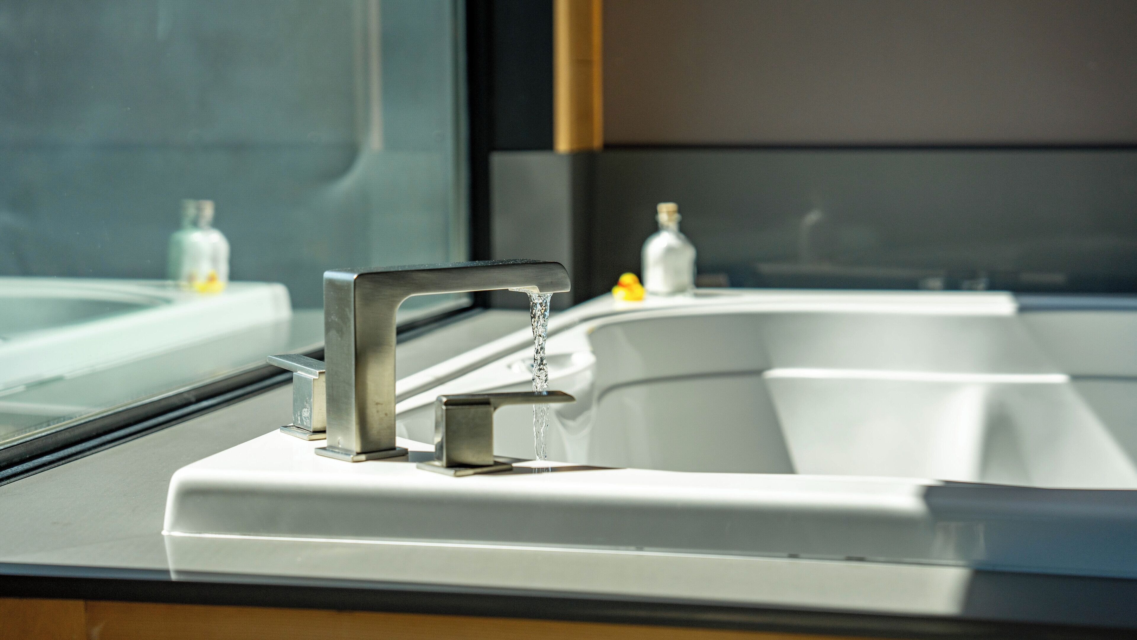 A modern bathroom with a stainless steel faucet, a white sink, and a window.