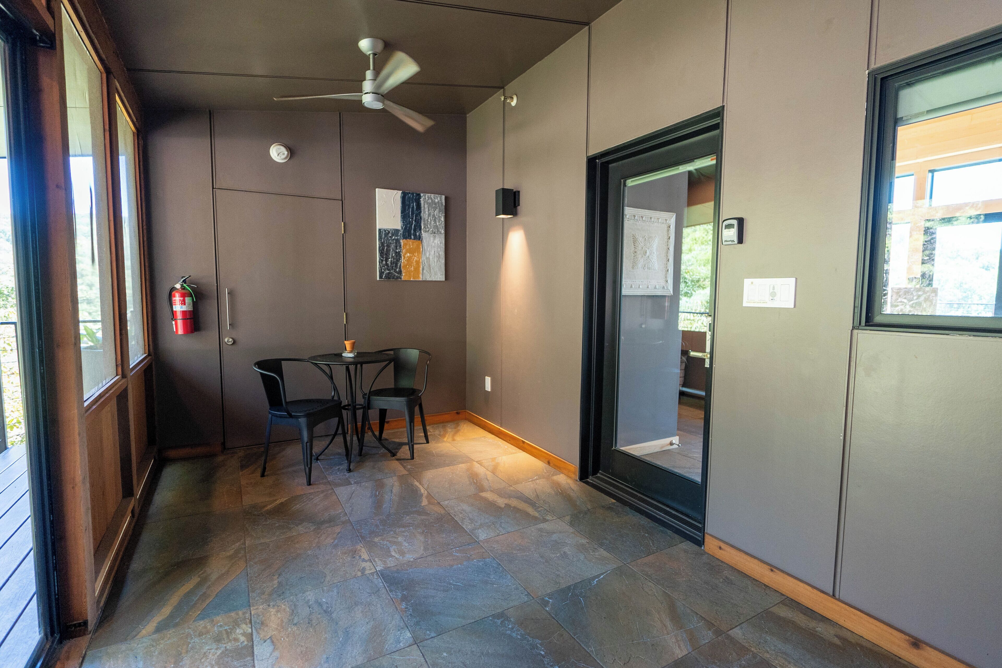 A modern interior with a ceiling fan, a table with chairs, and a fire extinguisher mounted on the wall.