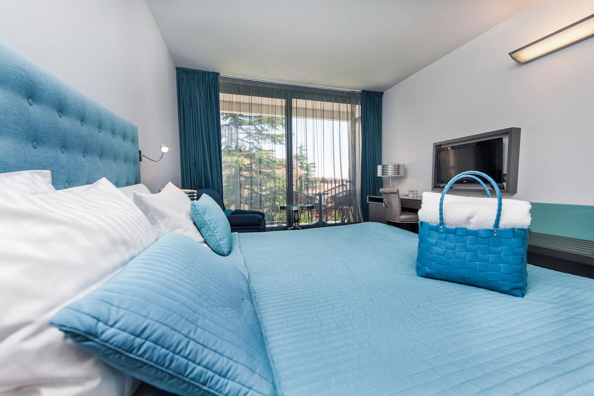 Ein Hotelzimmer mit einem großen Bett, einem Fernseher, einem Schreibtisch und einem Balkon mit Aussicht.