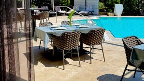 Een eetgedeelte bij het zwembad met tafels voor twee personen, rieten stoelen en een goed uitzicht op het zwembad.