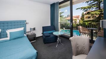 Una camera d'hotel con un letto grande, un divano, un tavolino e un balcone con vista sulla piscina.