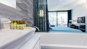 Een moderne badkamer met een badkuip, een wastafel met toiletartikelen en een groot raam met gordijnen.