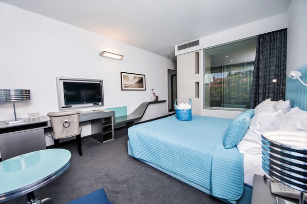 Habitación de hotel con cama, escritorio, silla, televisor y un ventanal grande.
