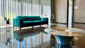 Een moderne lobby met een turquoise bank, een glimmende salontafel en een groot raam met transparante gordijnen.