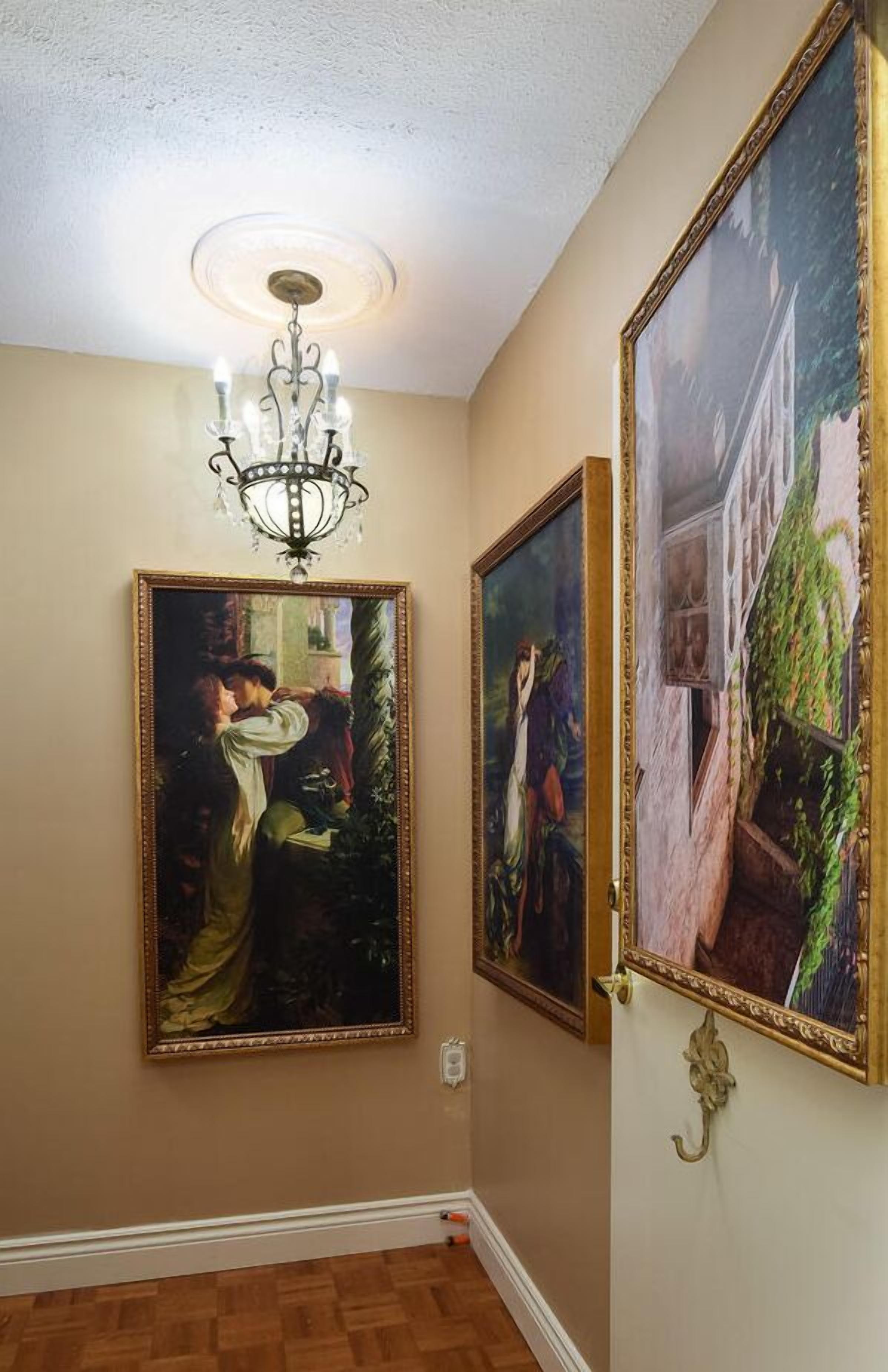 A hallway with a chandelier, two framed paintings, and a wooden floor.