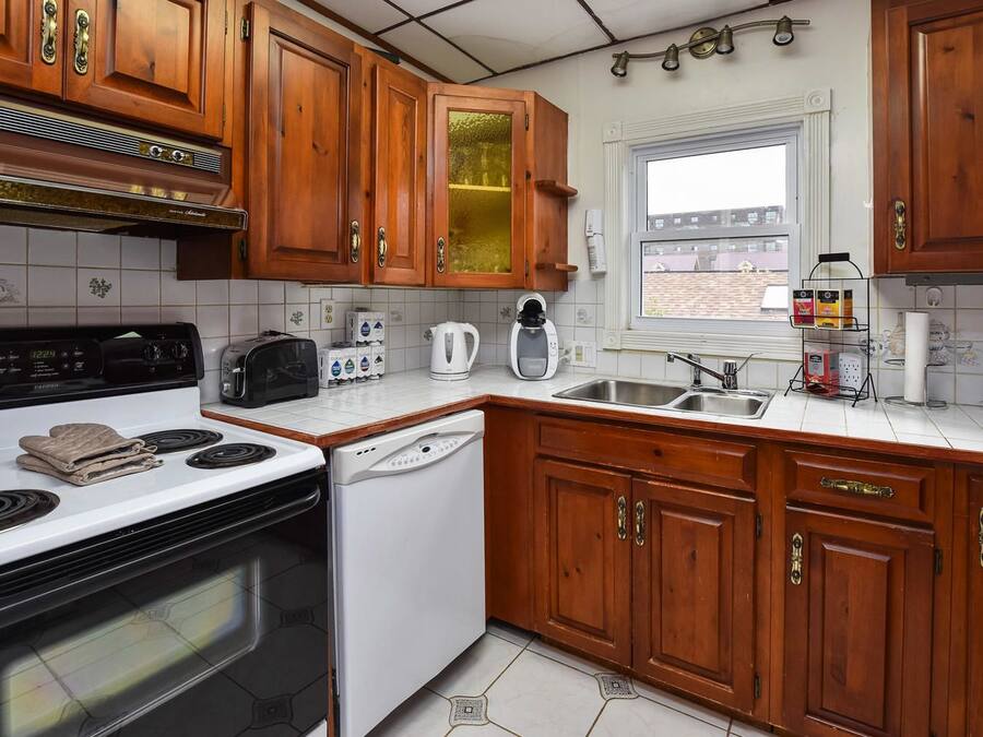 A kitchen with wooden cabinets, a white stove, a dishwasher, and a window with a view of buildings outside.