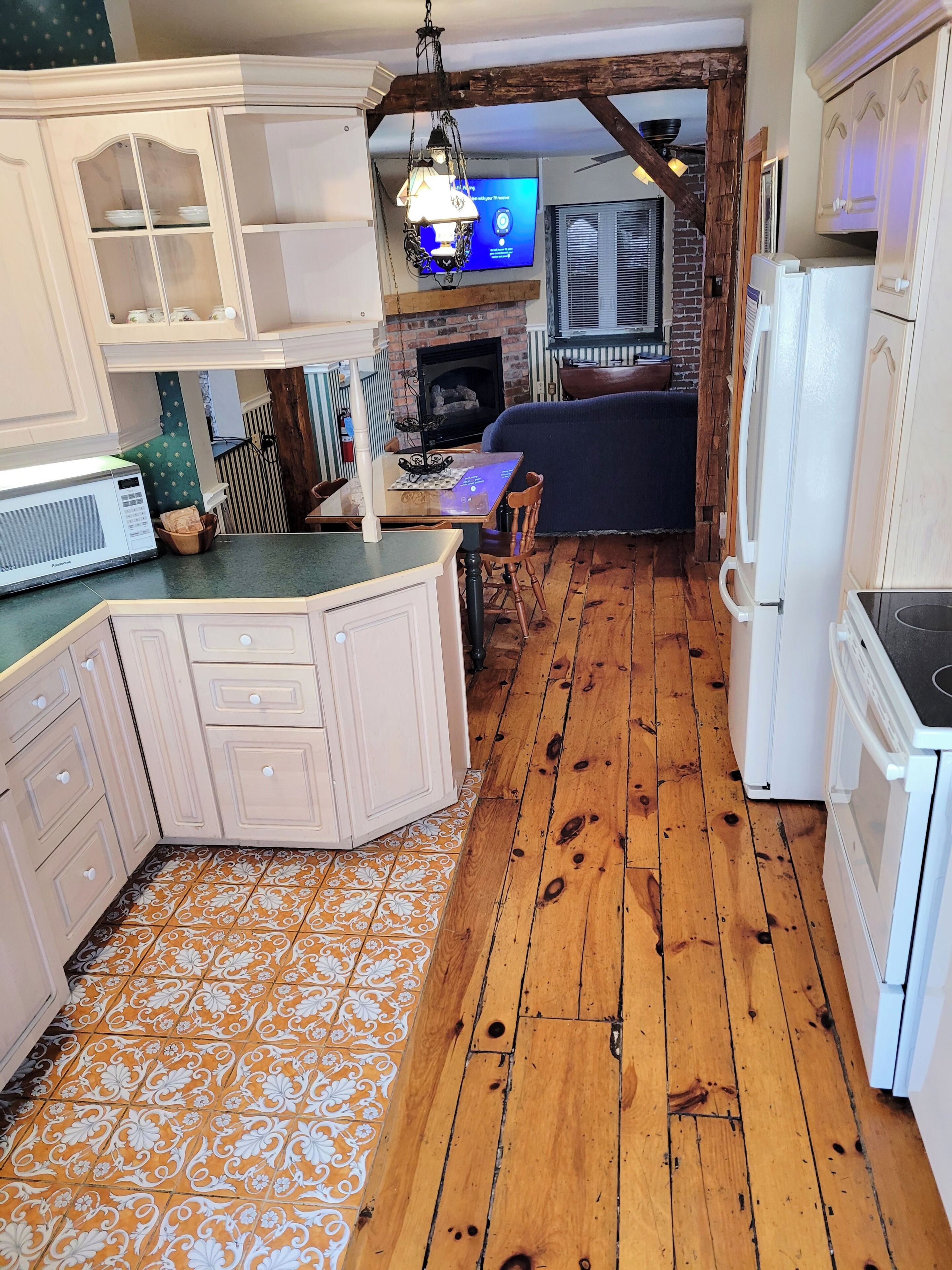 Una cocina con suelo de madera, microondas, refrigerador, mesa de comedor con sillas y televisión.