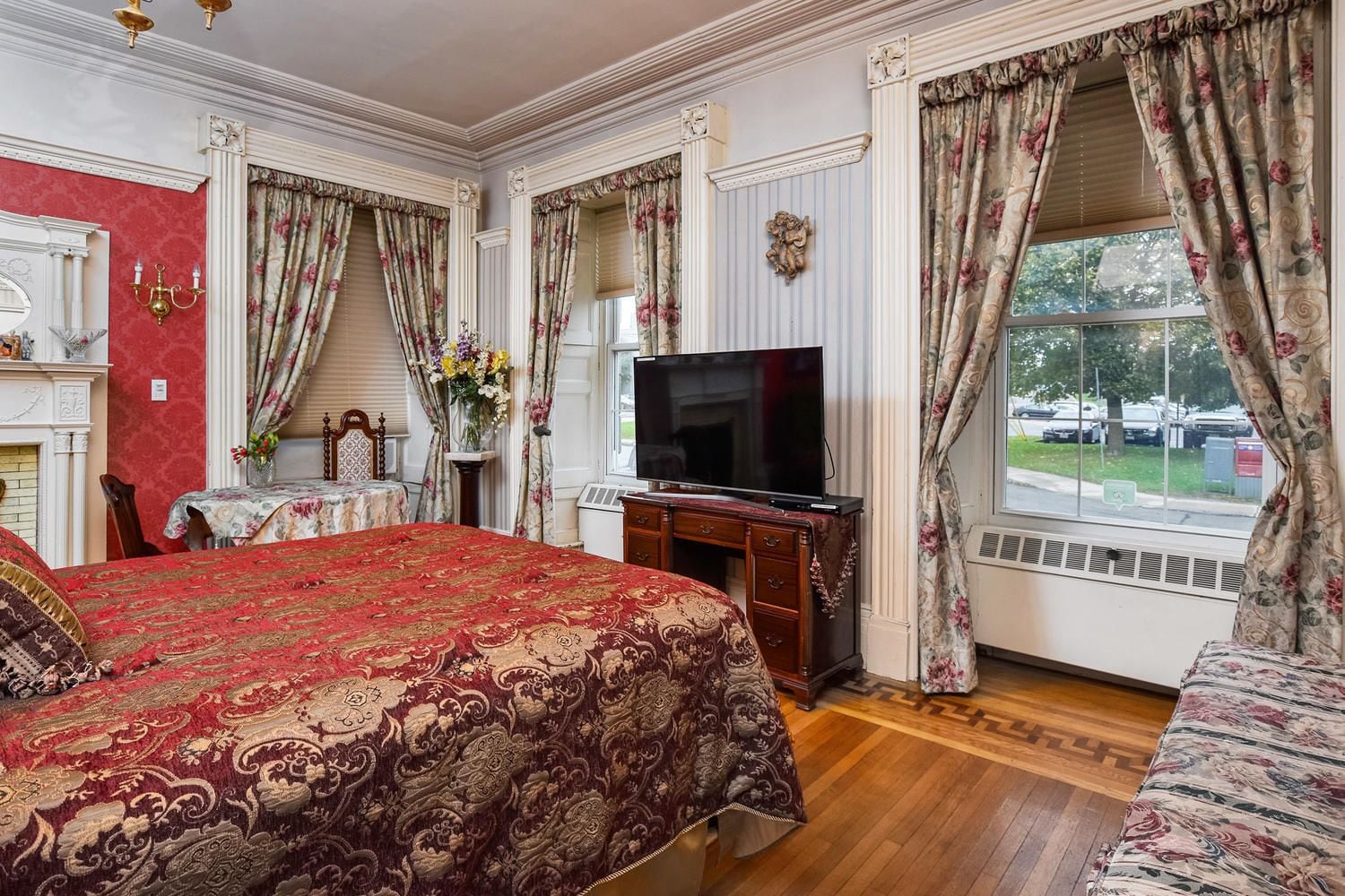 A hotel room with a large bed, a television, a desk with a chair, and a window with curtains.