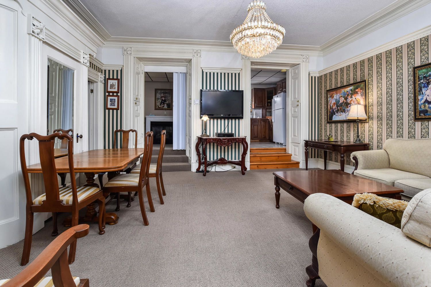 A spacious living room with a dining area, a chandelier, and a television.