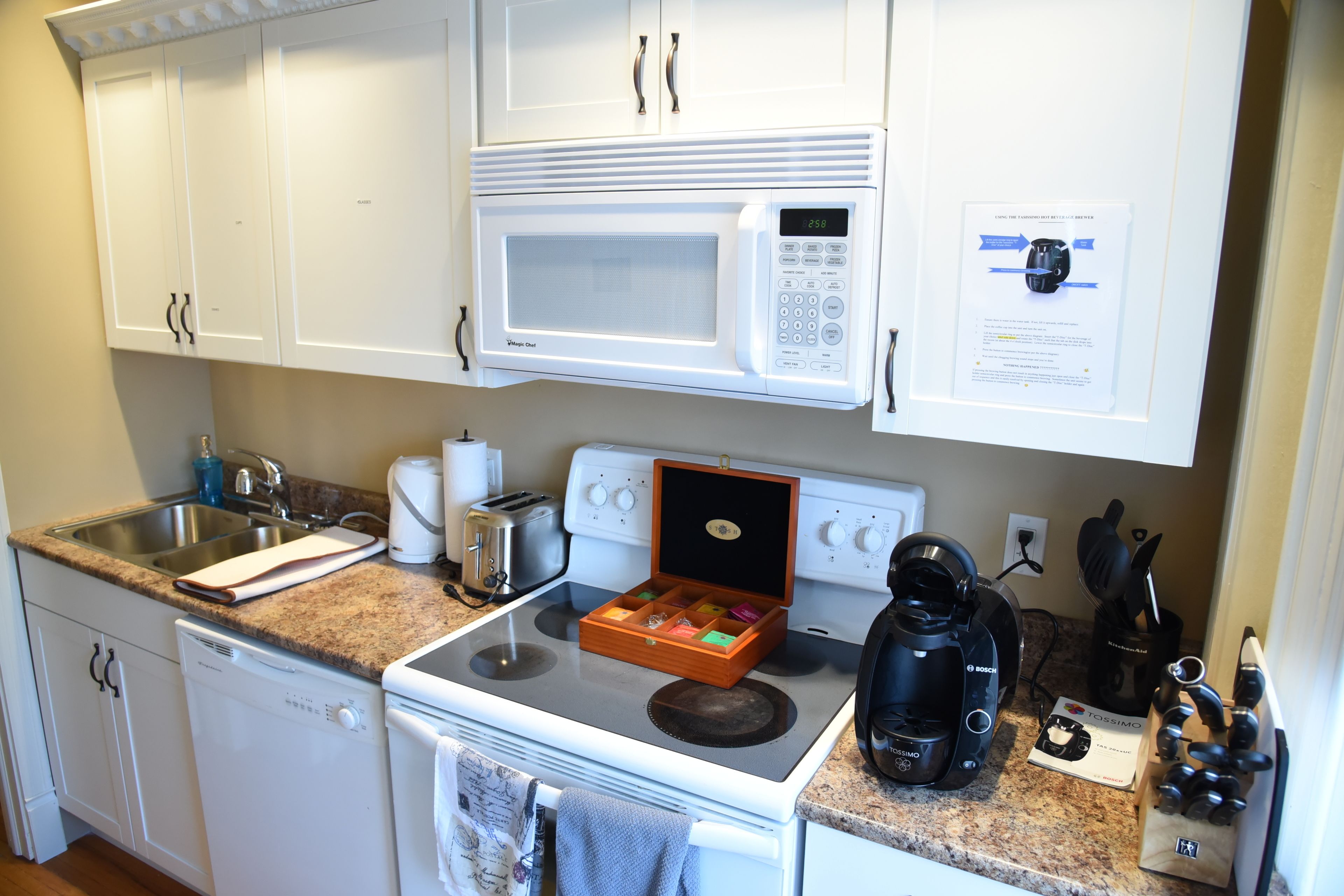 Una cocina con armarios blancos, microondas, tostadora, cafetera y escurreplatos.