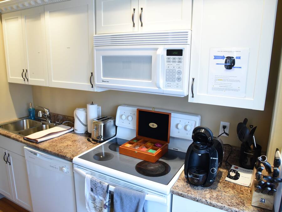 Una cocina con armarios blancos, microondas, tostadora, cafetera y escurreplatos.