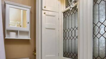 A bathroom with a toilet, a white cabinet with a mirror, a chandelier, and a window with decorative glass.