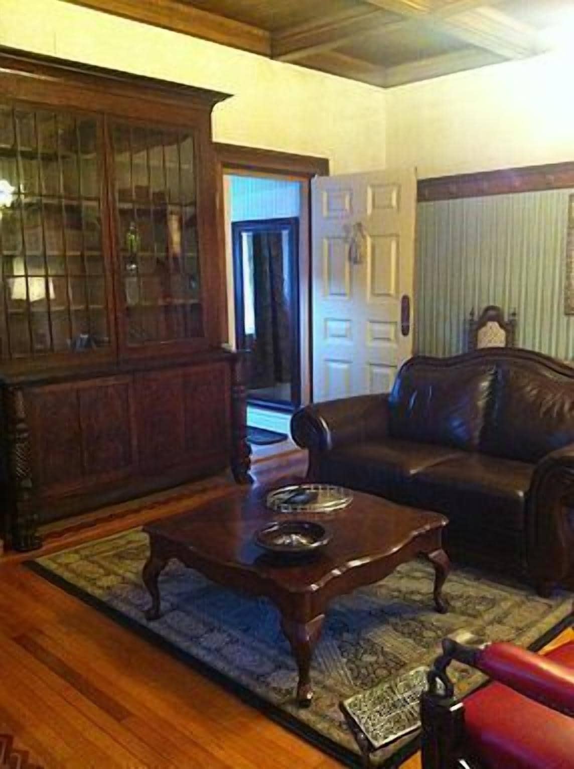 A living room with a dark wooden coffee table, a leather sofa, and a wooden cabinet with glass doors.