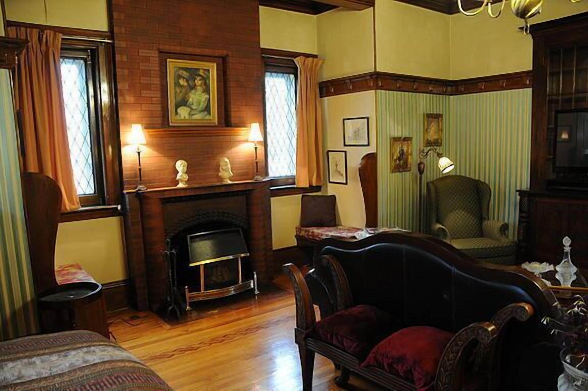 A traditional room with a fireplace, wooden flooring, a large armchair, and a dining table.