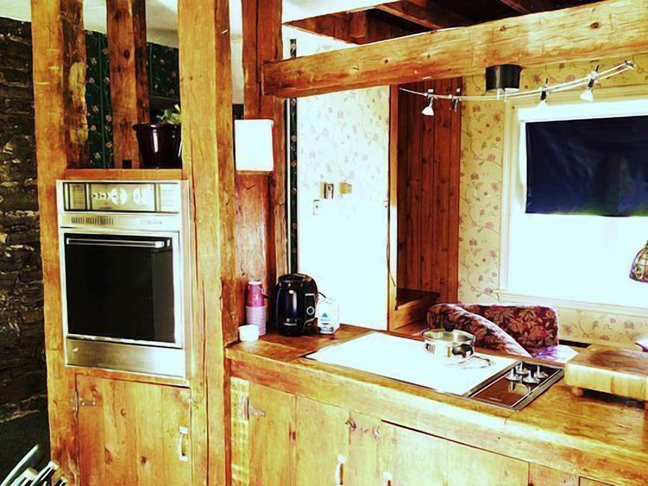 A rustic wooden cabin with a built-in stove, a sink, and a window with curtains.
