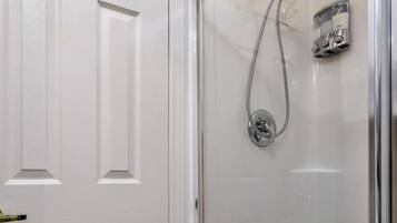 Un baño con ducha acristalada, una puerta blanca con pomos de latón y un pequeño perchero sobre la puerta.