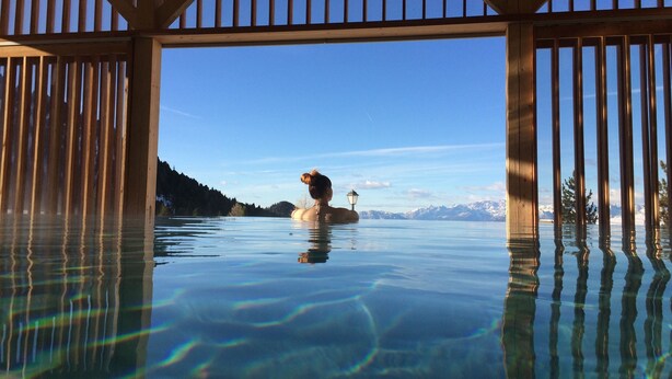 Duidelijk zicht op een houten terras met een glazen balustrade, uitkijkend over een rustig waterlichaam met iemand zittend op een drijvend platform.